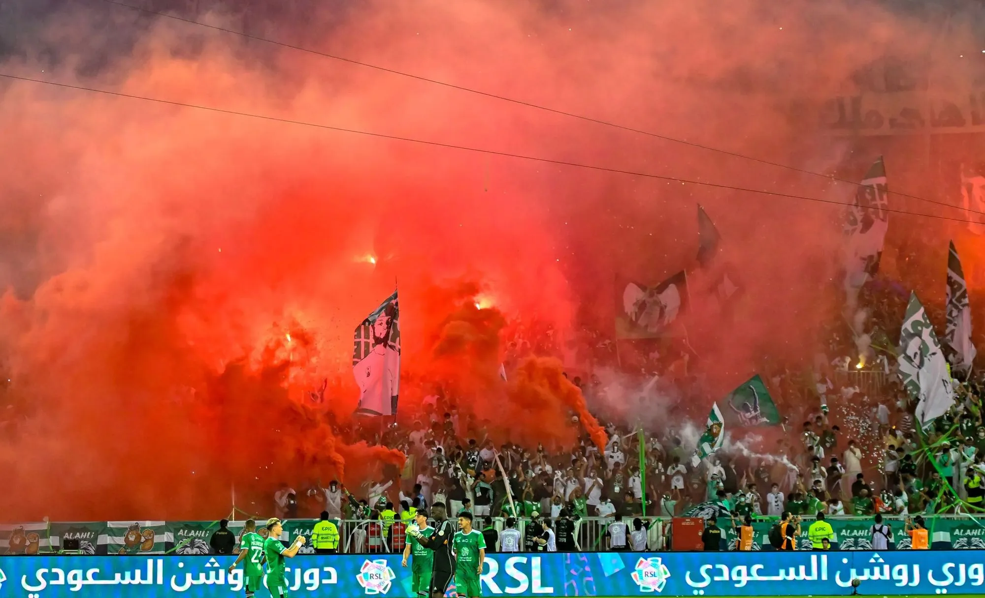 Al Ahli fans with red smoke and flags cheering passionately.